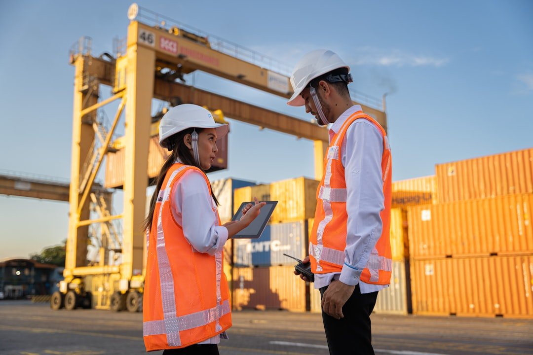 Logistics staff in high-visibility vests reviewing cargo documentation on a tablet at a container yard
